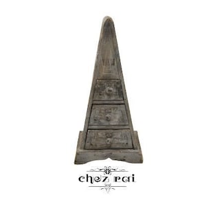 May include: A wooden pyramid-shaped cabinet with four drawers. The cabinet is painted in a distressed grey finish and has a decorative design on the front.