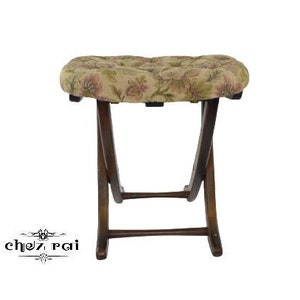 Puede incluir: Un taburete plegable de madera marrón con un cojín estampado floral. El taburete tiene un diseño sencillo y es perfecto para asientos adicionales.