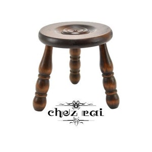 May include: A dark brown wooden stool with three turned legs. The stool has a round top with a slightly raised center.