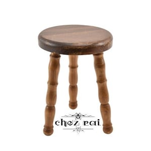 May include: A wooden stool with a round seat and three legs. The stool is made of dark brown wood and has a simple design.