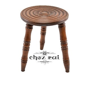 May include: A wooden stool with three legs and a round top. The top has a concentric circle design.
