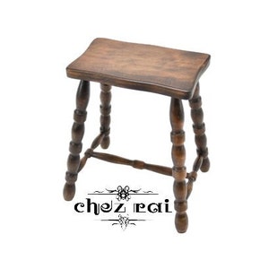 Puede incluir: Un taburete de madera con acabado marrón y patas torneadas. El taburete tiene un asiento rectangular y un diseño sencillo.