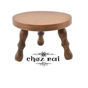 May include: A small wooden stool with a round top and three legs. The stool is brown and has a natural wood finish.
