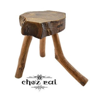 Könnte beinhalten: Ein rustikaler Holzhocker mit drei Beinen. Die Sitzfläche besteht aus einem dicken Stück Holz mit einer natürlichen, rauen Oberfläche.
