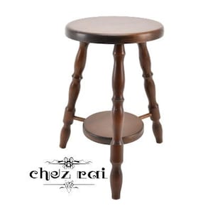 Könnte beinhalten: Ein dunkelbrauner Holzhocker mit einer runden Sitzfläche und einem unteren Regal. Der Hocker hat vier Beine und ein schlichtes Design.