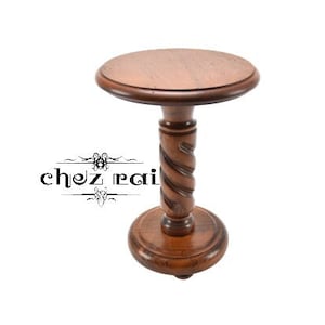 Puede incluir: Una mesa pequeña, redonda y de madera con una base de pedestal retorcido. La superficie de la mesa es de color marrón oscuro y la base es de un marrón más oscuro.