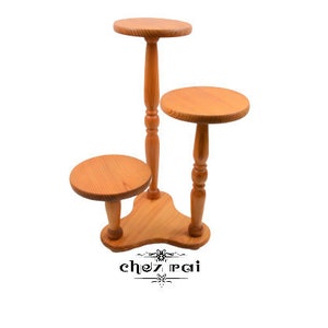 Puede incluir: Un soporte para plantas de madera de tres niveles con un acabado de madera natural. El soporte tiene una base triangular y tres estantes redondos.