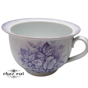 May include: A white ceramic teacup with a purple floral design. The cup has a wide, rounded bowl and a handle.