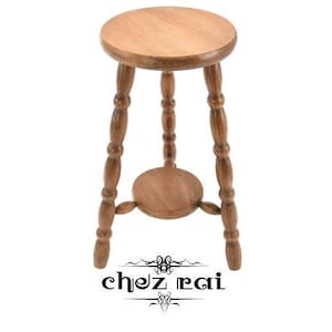 Op de afbeelding: Een houten kruk met een ronde bovenkant en drie gedraaide poten. De poten hebben een decoratief knopje aan de onderkant. De kruk is gemaakt van natuurlijk hout en heeft een lichtbruine afwerking.