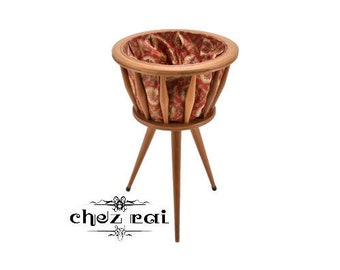 May include: A wooden plant stand with three legs and a round, fabric-lined basket. The basket has a red and brown floral pattern.