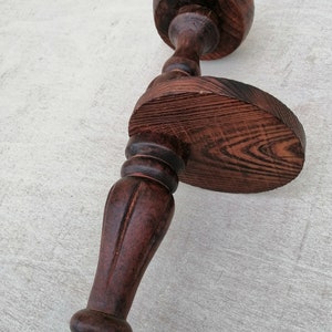 K&ouml;nnte beinhalten: Ein dunkelbrauner Kerzenhalter aus Holz mit runder Basis und einem hohen, geriffelten Stiel. Der Halter hat ein dekoratives Design und eine abgenutzte Oberfl&auml;che.