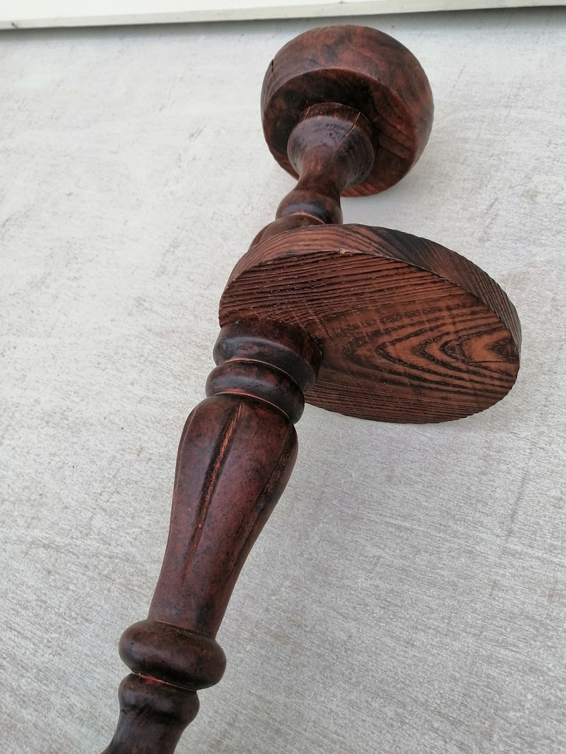 K&ouml;nnte beinhalten: Ein dunkelbrauner Kerzenhalter aus Holz mit runder Basis und einem hohen, geriffelten Stiel. Der Halter hat ein dekoratives Design und eine abgenutzte Oberfl&auml;che.