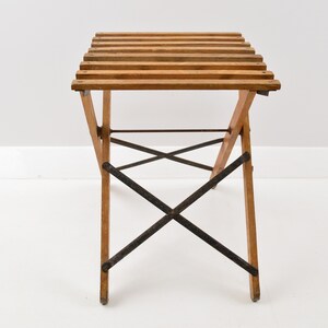 May include: A wooden folding table with a slatted top and black metal supports. The table is made of natural wood and has a rustic look.