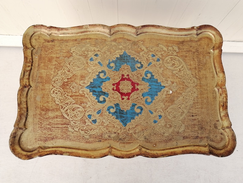 May include: A gold tray with a decorative design featuring blue, red, and gold accents. The tray has a scalloped edge and a distressed finish.