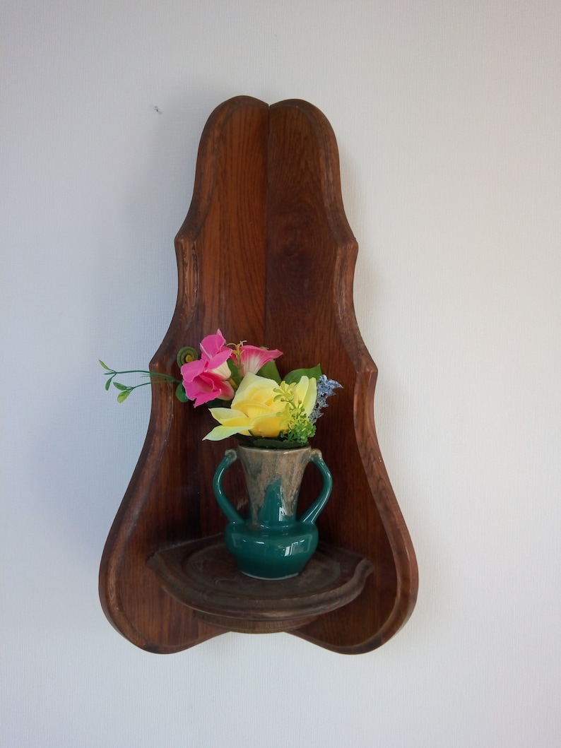 May include: A wooden corner shelf with a carved design, featuring a green ceramic vase with pink and yellow flowers.