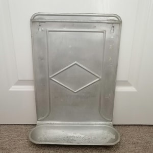 Puede incluir: Un estante de pared de metal plateado con un patr&oacute;n de diamante y un peque&ntilde;o estante en la parte inferior.