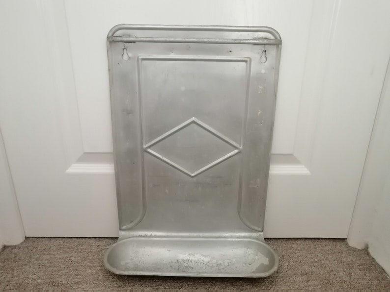 Puede incluir: Un estante de pared de metal plateado con un patr&oacute;n de diamante y un peque&ntilde;o estante en la parte inferior.