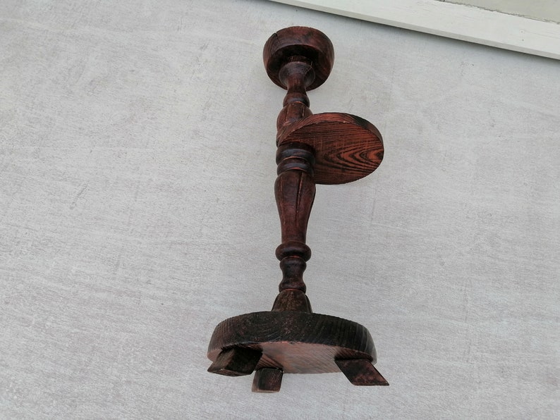 K&ouml;nnte beinhalten: Ein dunkelbrauner Pflanzenst&auml;nder aus Holz mit einer runden Oberseite und drei Beinen. Der St&auml;nder hat ein dekoratives Design an den Beinen und der Oberseite.