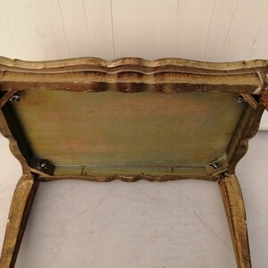 May include: A small, antique, wooden table with a gold finish. The table has a scalloped edge and four legs. The table top is painted in shades of green, yellow, and brown.