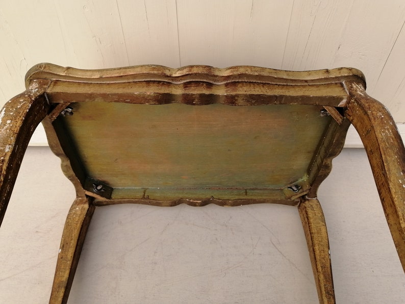 May include: A small, antique, wooden table with a gold finish. The table has a scalloped edge and four legs. The table top is painted in shades of green, yellow, and brown.