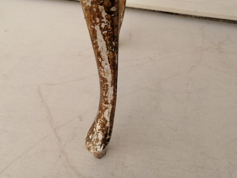 May include: Close-up of a wooden table leg with a distressed white paint finish. The leg is carved with a decorative design and has a slightly curved shape.