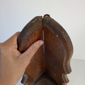 May include: A wooden corner shelf with a simple design. The shelf is made of dark wood and has a rounded edge. It has a small metal hook at the top.
