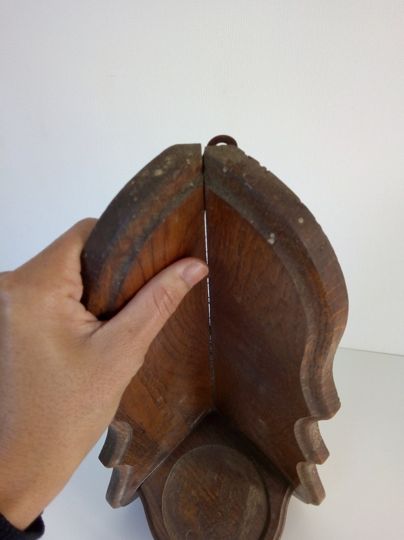 May include: A wooden corner shelf with a simple design. The shelf is made of dark wood and has a rounded edge. It has a small metal hook at the top.
