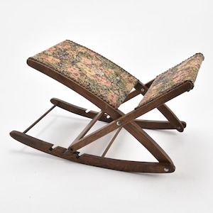 May include: A wooden folding footstool with a floral patterned fabric top. The footstool has a rocking base.