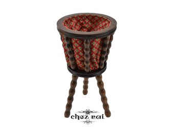 May include: A wooden planter with a red and green patterned fabric lining. The planter has three legs and is made of dark wood.