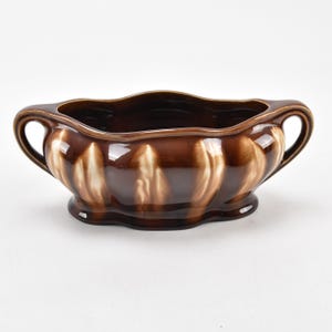 May include: A brown ceramic planter with white accents and two handles. The planter has a wavy rim and a rounded base.