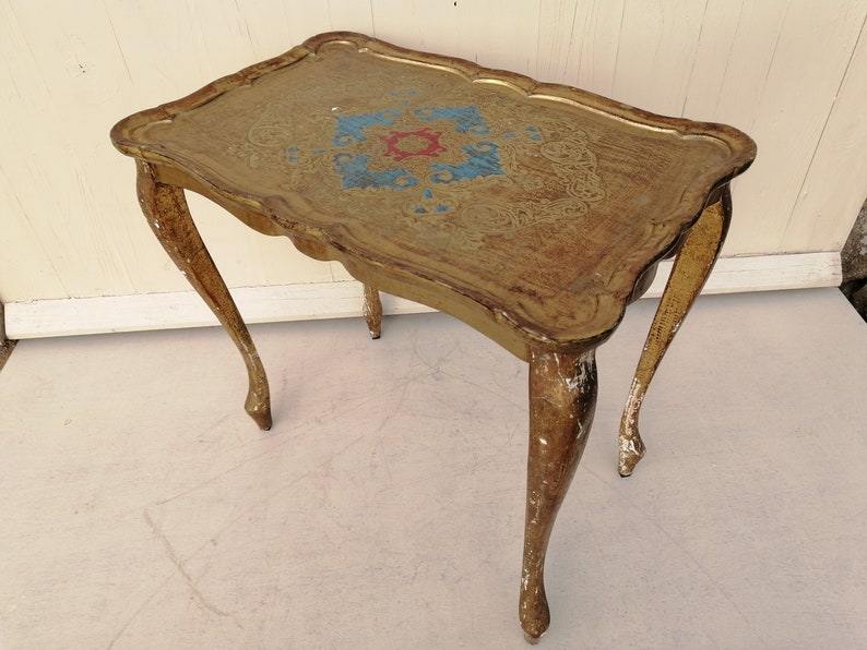 May include: A gold-painted side table with a decorative, ornate top and three legs. The table has a distressed finish, giving it a vintage look.