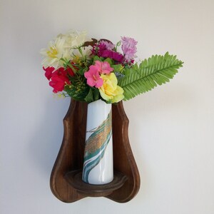 May include: A wooden shelf shaped like a violin with a white vase with green and gold designs holding a bouquet of pink, yellow, white, and red flowers.
