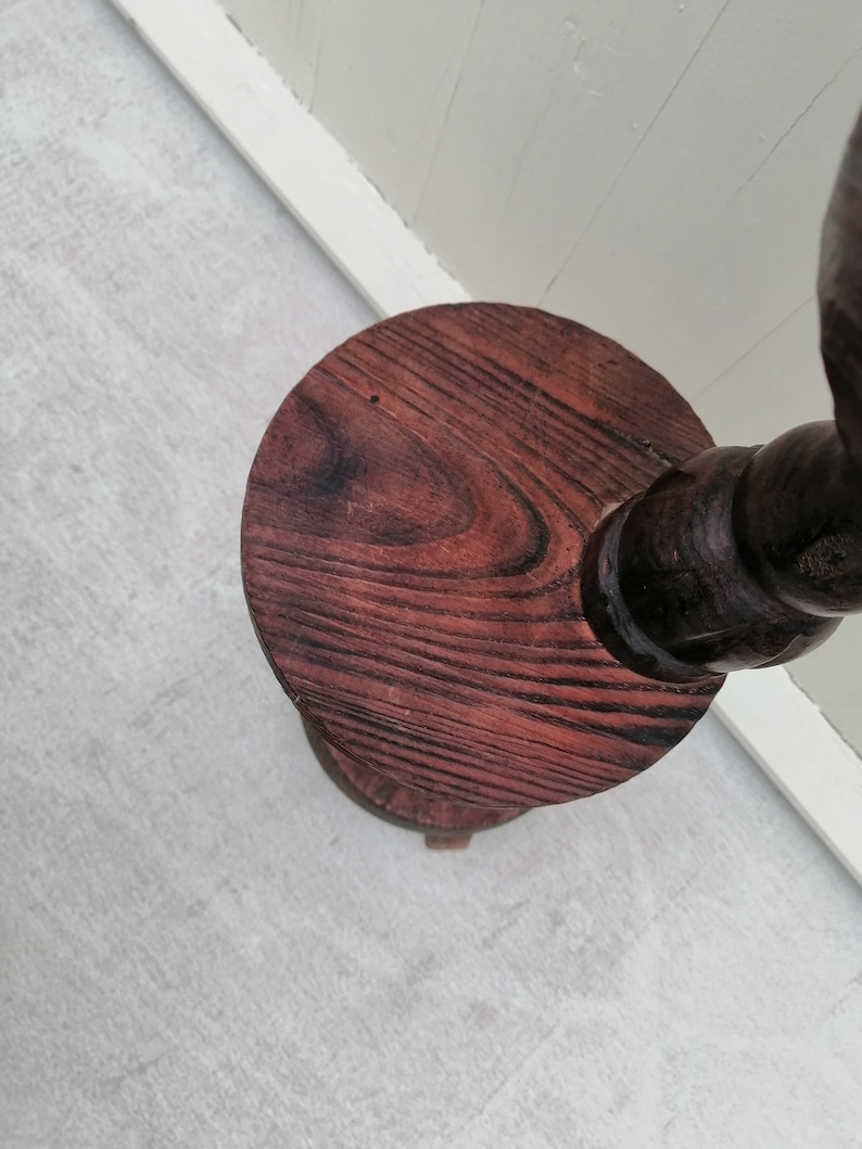 K&ouml;nnte beinhalten: Ein Holzsockel mit runder Oberseite und gedrehtem Fu&szlig;. Der Sockel ist in einem dunklen Rotbraun gebeizt.