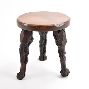 May include: A wooden stool with a round top and three legs. The legs are carved to resemble tree roots.