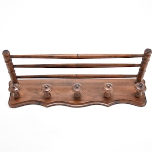 Puede incluir: Un perchero de pared de madera marrón oscuro. Cuenta con tres barras horizontales en la parte superior y cinco pomos decorativos en la parte inferior. El perchero tiene un borde festoneado y está diseñado para colgar abrigos u otros objetos.