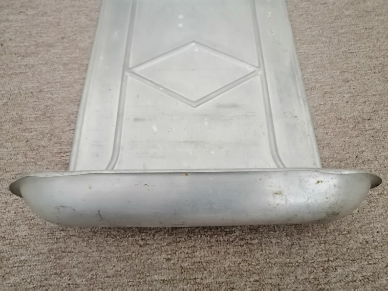 Puede incluir: Una bandeja de metal plateado con un patr&oacute;n de diamante en relieve en la superficie. La bandeja tiene un borde elevado alrededor del borde y un borde curvo en un lado.