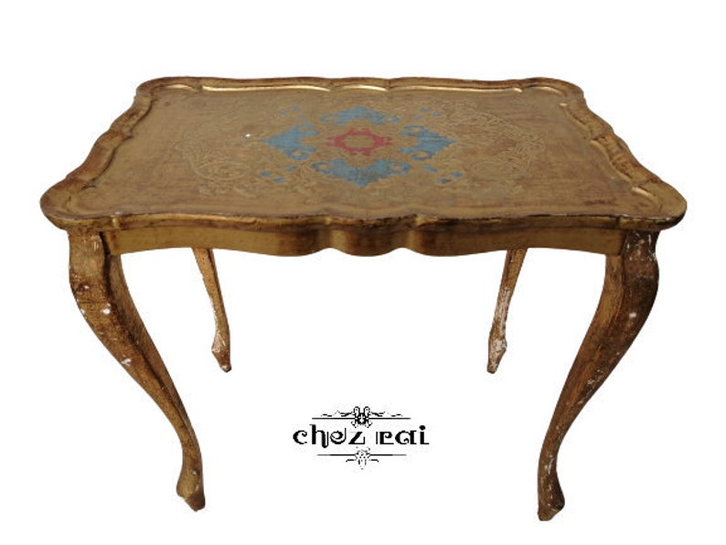 May include: A gold-painted wooden table with a carved top and ornate legs. The table top has a decorative design in blue, red, and gold.