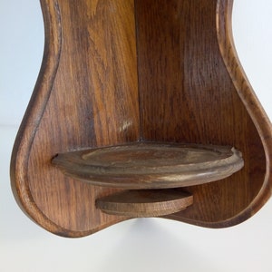 May include: A wooden corner shelf with a rounded, teardrop shape. The shelf has a small, round ledge on the bottom.
