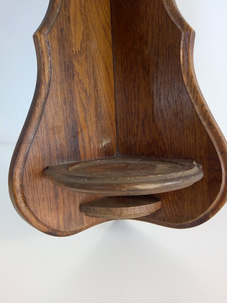 May include: A wooden corner shelf with a rounded, teardrop shape. The shelf has a small, round ledge on the bottom.