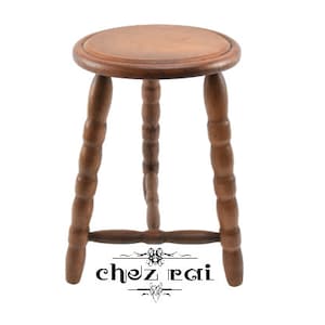 May include: A wooden stool with a round seat and three turned legs. The stool is made of dark brown wood and has a simple, rustic design.