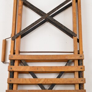 May include: A wooden folding step stool with black metal bracing and a wooden handle. The stool has four steps and is in a folded position.