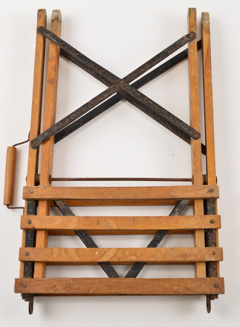 May include: A wooden folding step stool with black metal bracing and a wooden handle. The stool has four steps and is in a folded position.