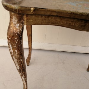 May include: A gold-painted side table with three legs. The table has a distressed finish with white paint showing through the gold.
