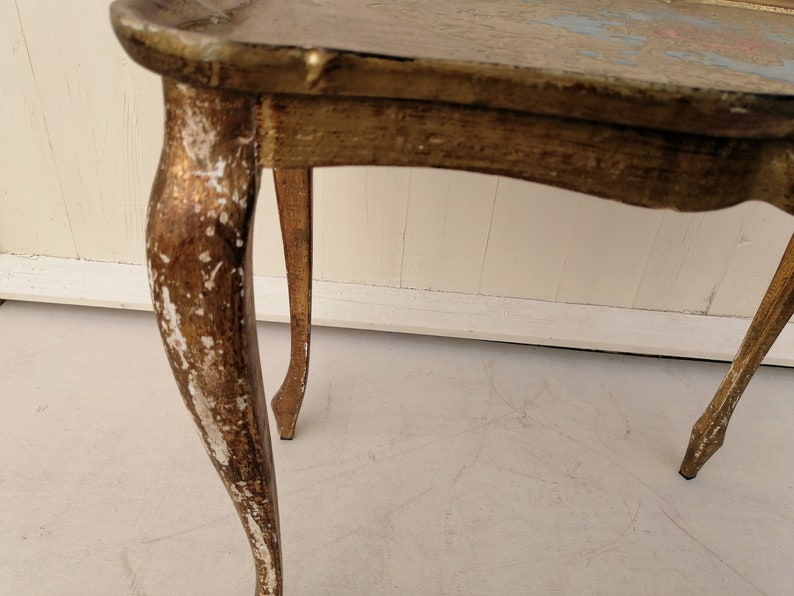 May include: A gold-painted side table with three legs. The table has a distressed finish with white paint showing through the gold.