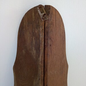 May include: The back of a wooden frame with a decorative, scalloped edge. The frame is made of two pieces of wood that are joined together with a metal hinge. The wood is a dark brown colour and has a natural wood grain.