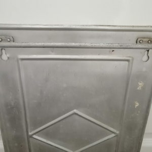 Puede incluir: Un estante de pared de metal plateado con un patr&oacute;n de diamante. El estante tiene dos agujeros en la parte superior y dos agujeros en la parte inferior para colgar.