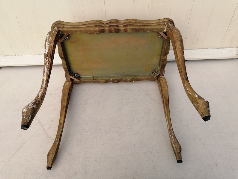 May include: A small, ornate, wooden table with a light brown finish and carved details. The table has four legs and a rectangular top.