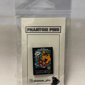 May include: A pin featuring a colourful graphic from the Sega Genesis game, ToeJam & Earl. The pin is rectangular with a black border and the game's logo. The pin is on a white card with "Phantom Pins" printed on it.