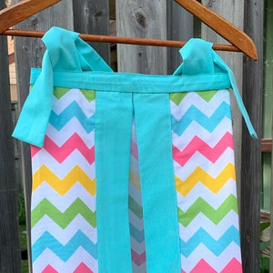 May include: A turquoise diaper caddy with a chevron pattern in pink, yellow, green, and blue. The caddy has two straps and a center opening.