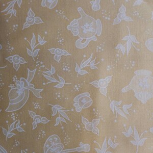 May include: A yellow fabric with a white floral pattern. The pattern includes teapots, flowers, and leaves.